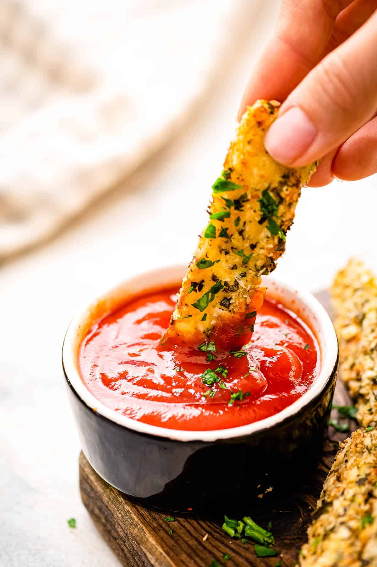 Hand dipping zucchini fry into a small bowl of ketchup