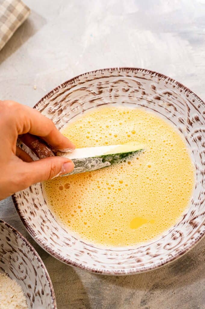 Handing dipping zucchini fry in egg