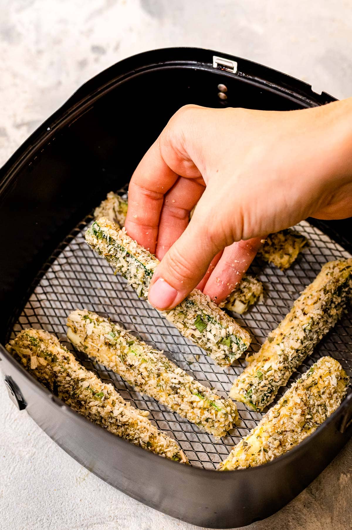 Hand placing a zucchini fry in air fryer basket
