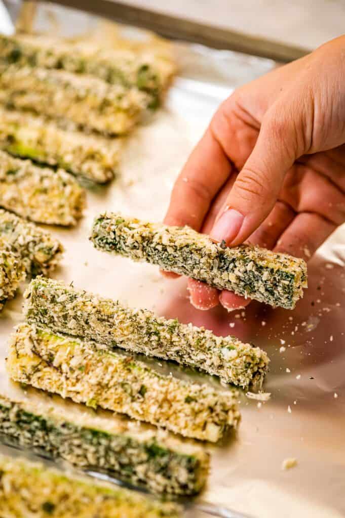 Hand placing zucchini fries on a lined baking sheet