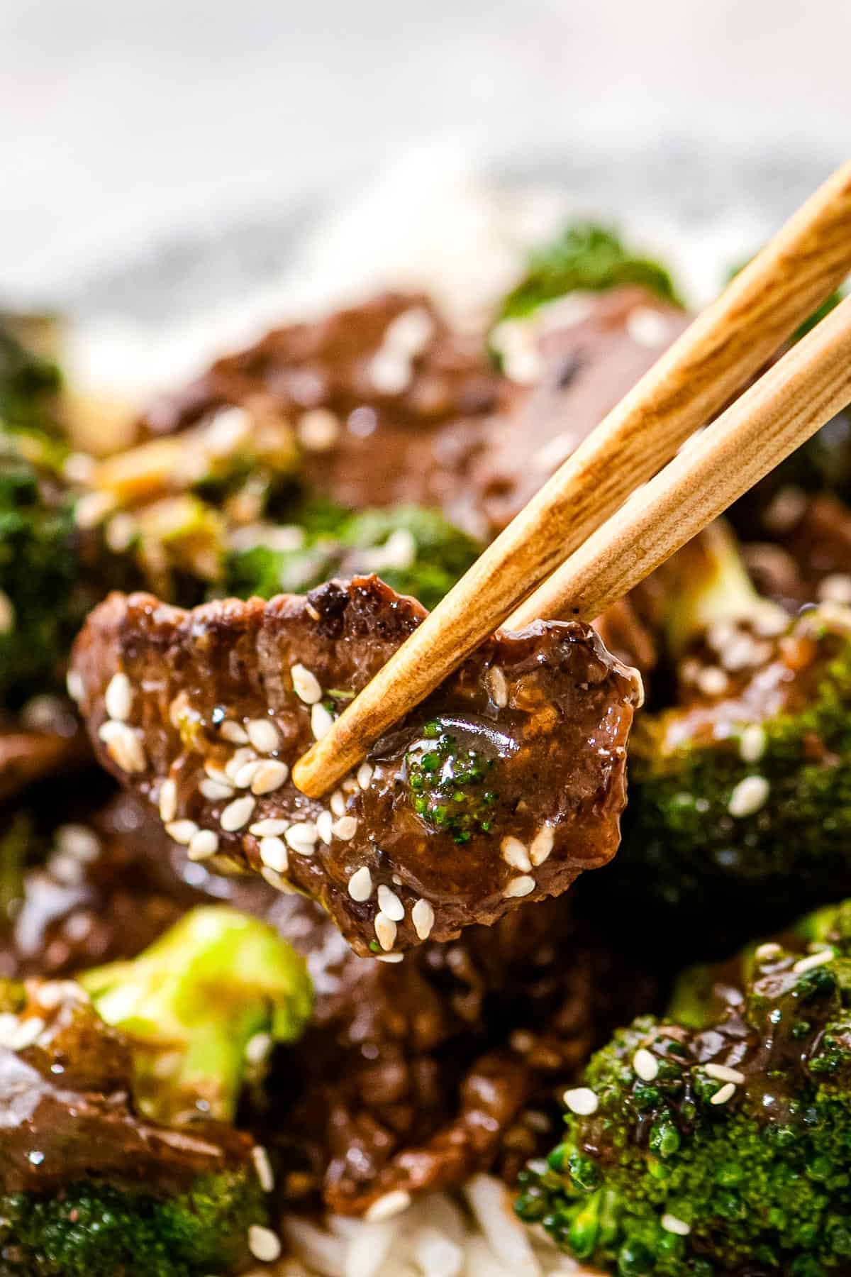 Chopstick holding a piece of beef and broccoli