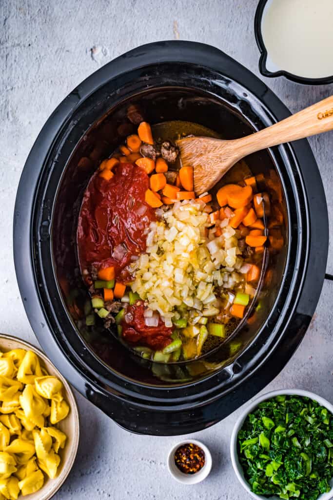 Black crock pot liner with carrots, tomatoes, spices, sausage and celery