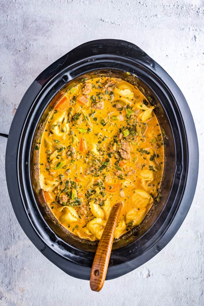 Wooden spoon in a crock pot with tortellini soup