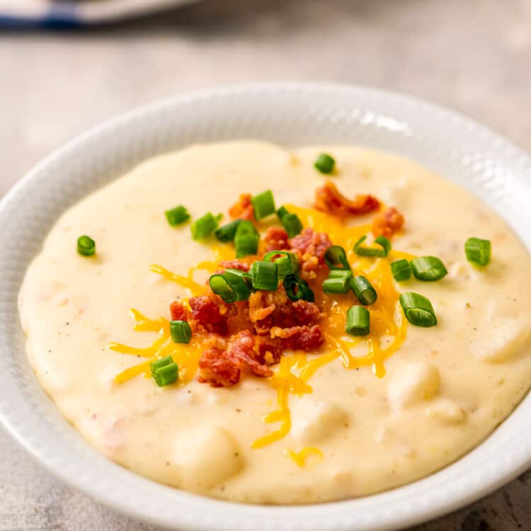 Crock Pot Potato Soup in white bowl with bacon, cheese and green onions on top
