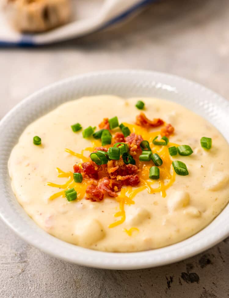 Crock Pot Potato Soup in white bowl with bacon, cheese and green onions on top