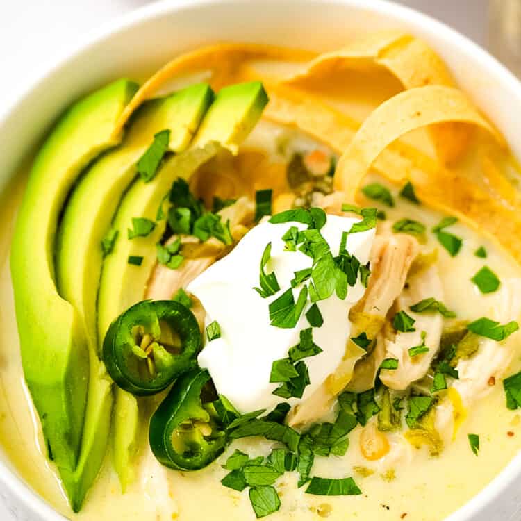 Overhead image of white bowl with Crock Pot White Chicken Chili topped with sour cream, tortilla strips, sliced avocado