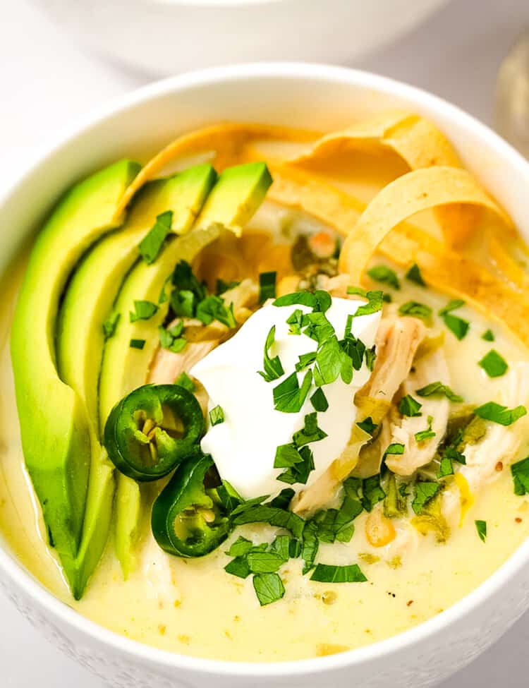 Overhead image of white bowl with Crock Pot White Chicken Chili topped with sour cream, tortilla strips, sliced avocado