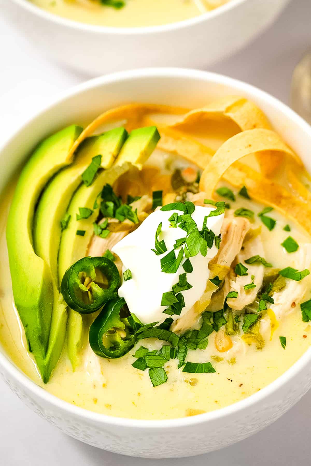 Overhead image of white bowl with Crock Pot White Chicken Chili topped with sour cream, tortilla strips, sliced avocado