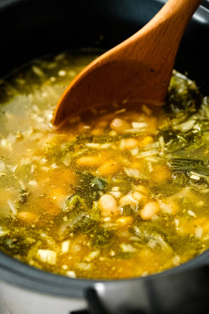 Spoon stirring soup ingredients in black crock pot