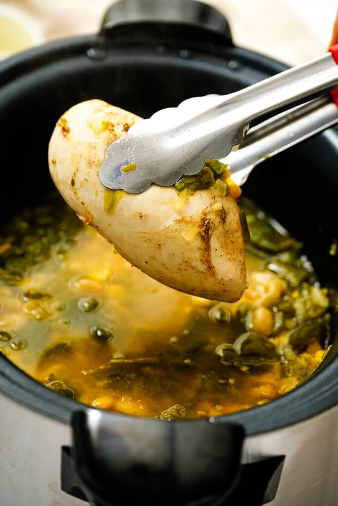 Metal tongs lifting chicken breast out of crock pot