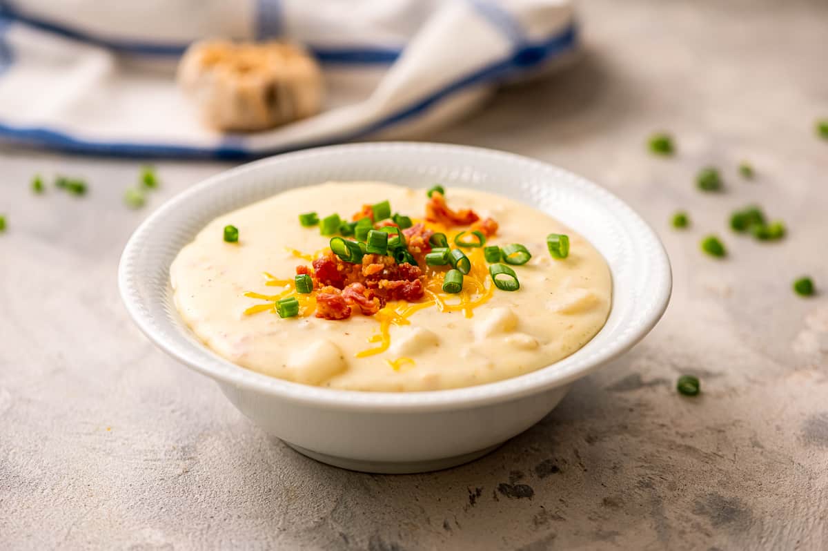 White bowl of potato soup topped with cheese, bacon and green onions