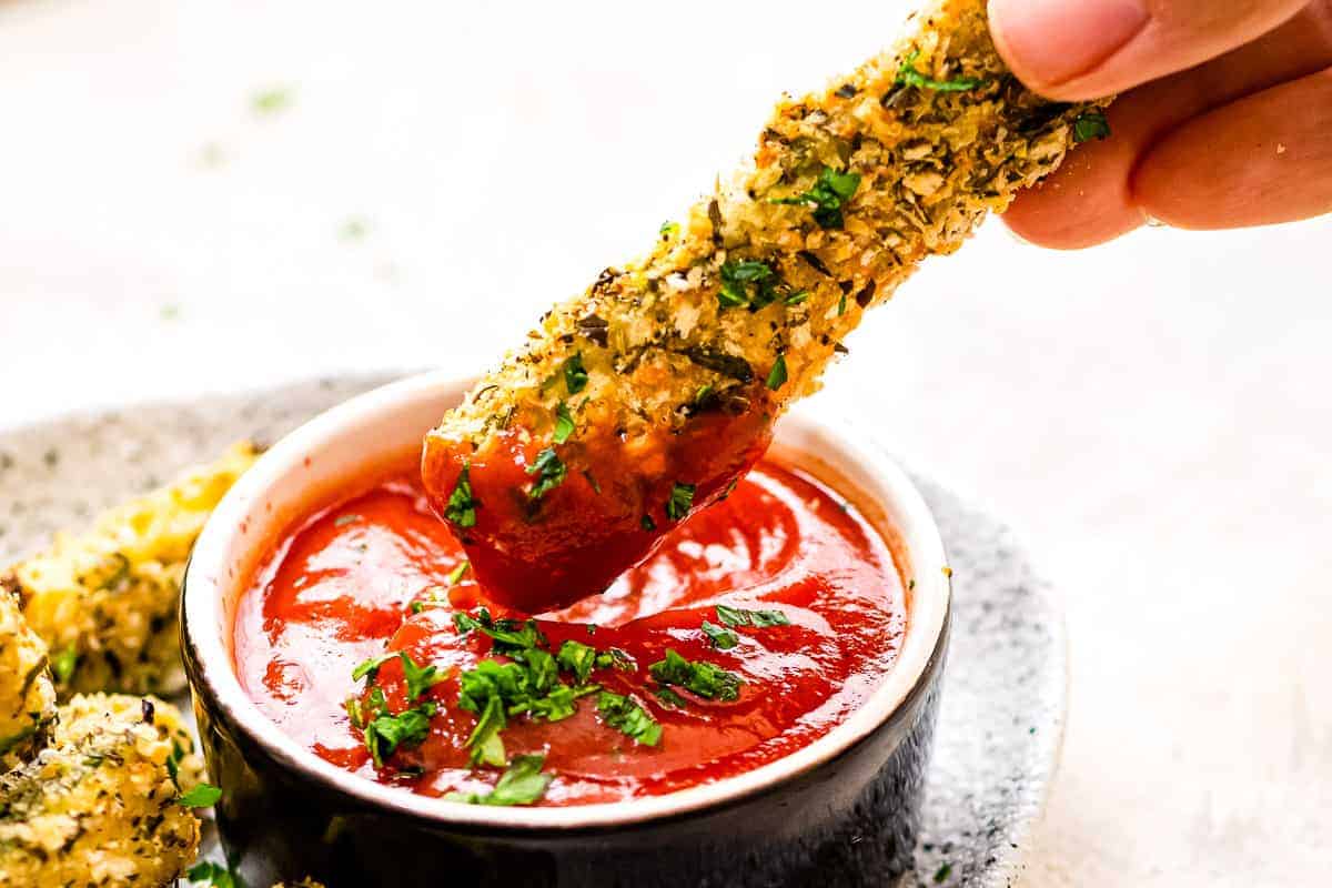 Hand dipping a zucchini fry into ketchup