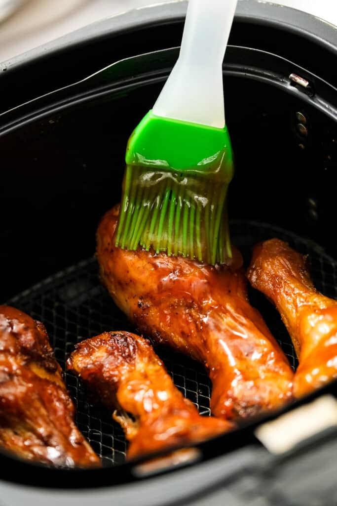 Chicken legs being basted with BBQ sauce in Air Fryer Basket