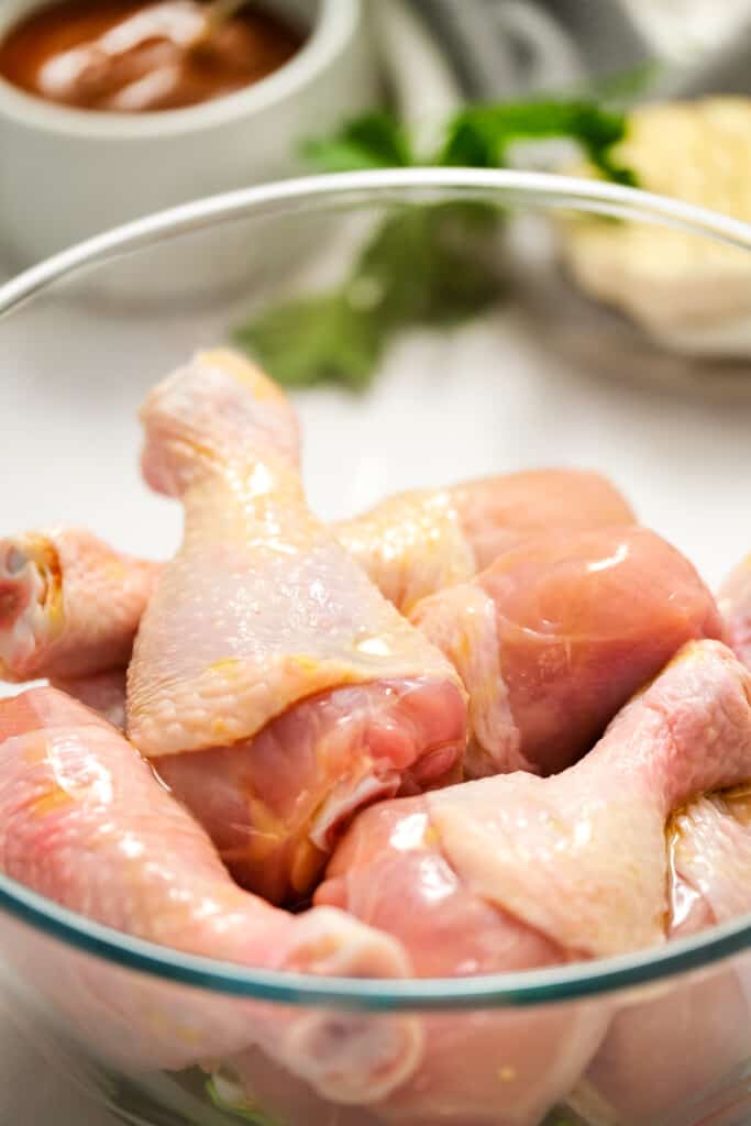 Glass bowl with chicken legs with olive oil on them