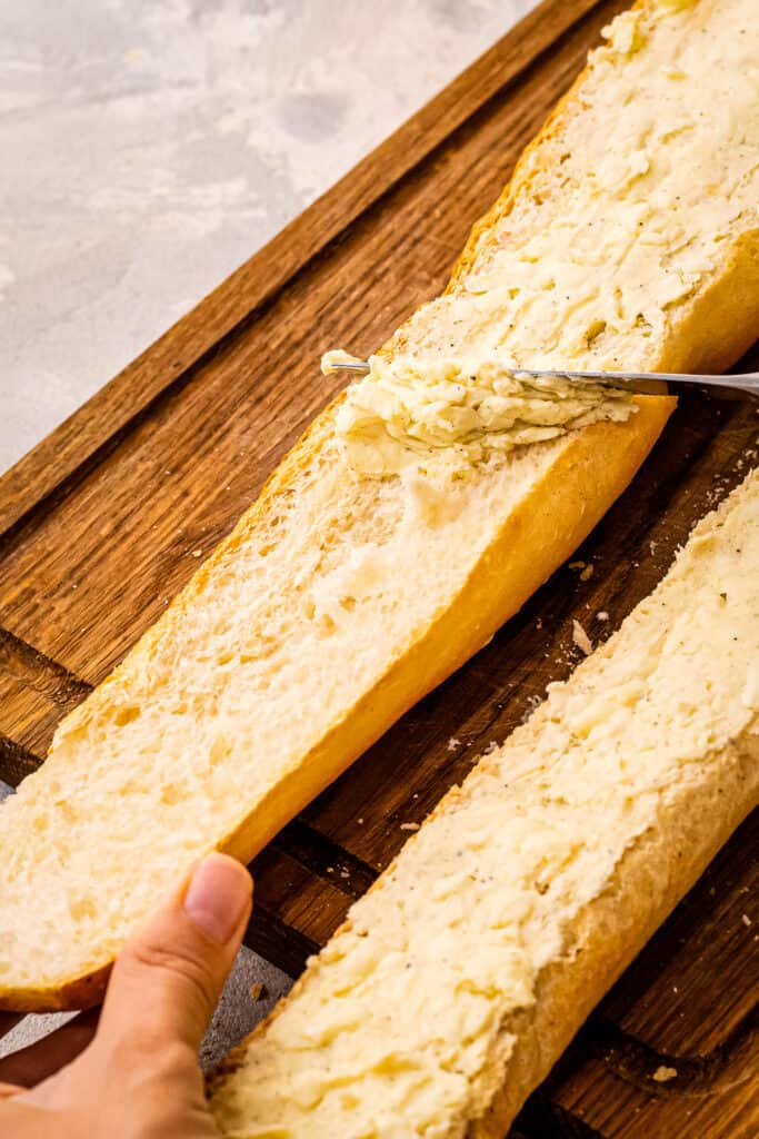 Butter knife putting on garlic butter topping on French Bread