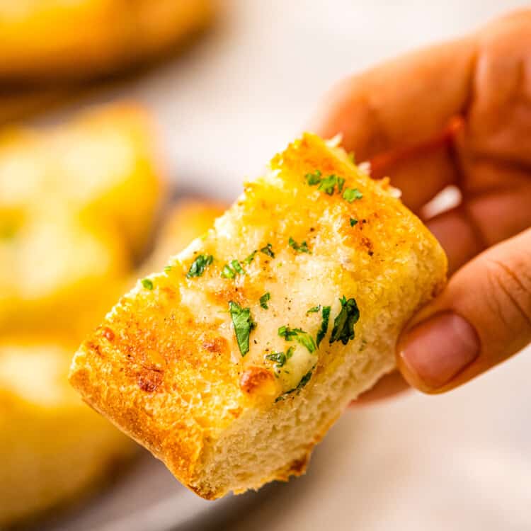 Piece of garlic bread with chopped parsley in hand