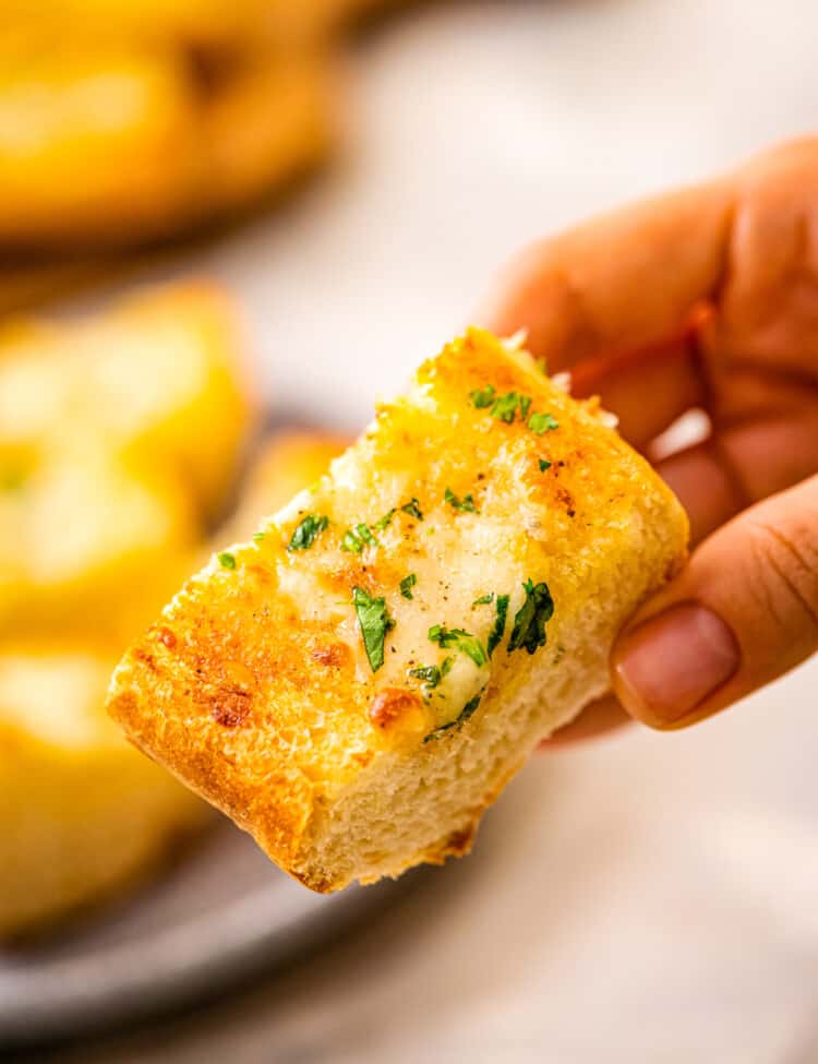 Piece of garlic bread with chopped parsley in hand