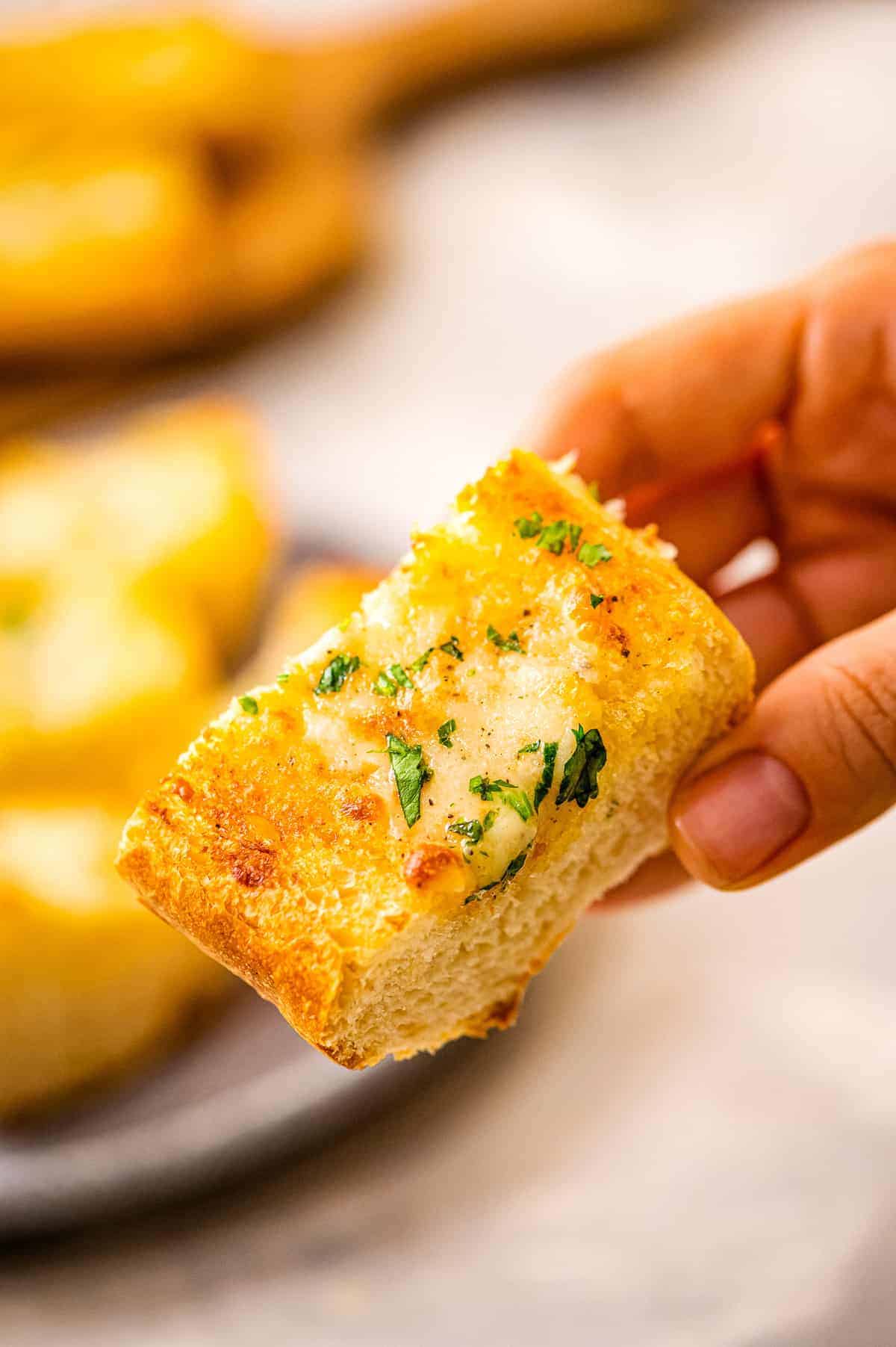 Piece of garlic bread with chopped parsley in hand