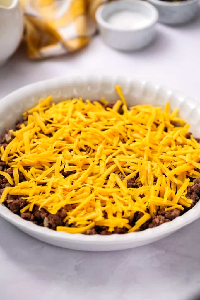 White pie plate with ground beef and cheddar cheese