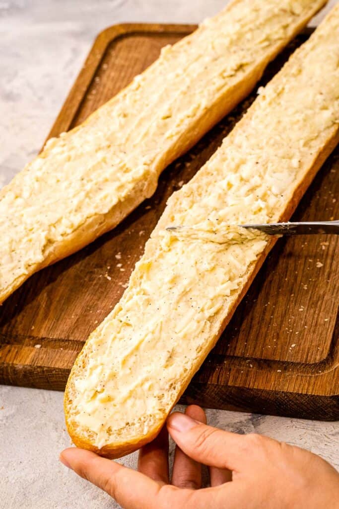 Knife spreading garlic butter on a slice of French Bread