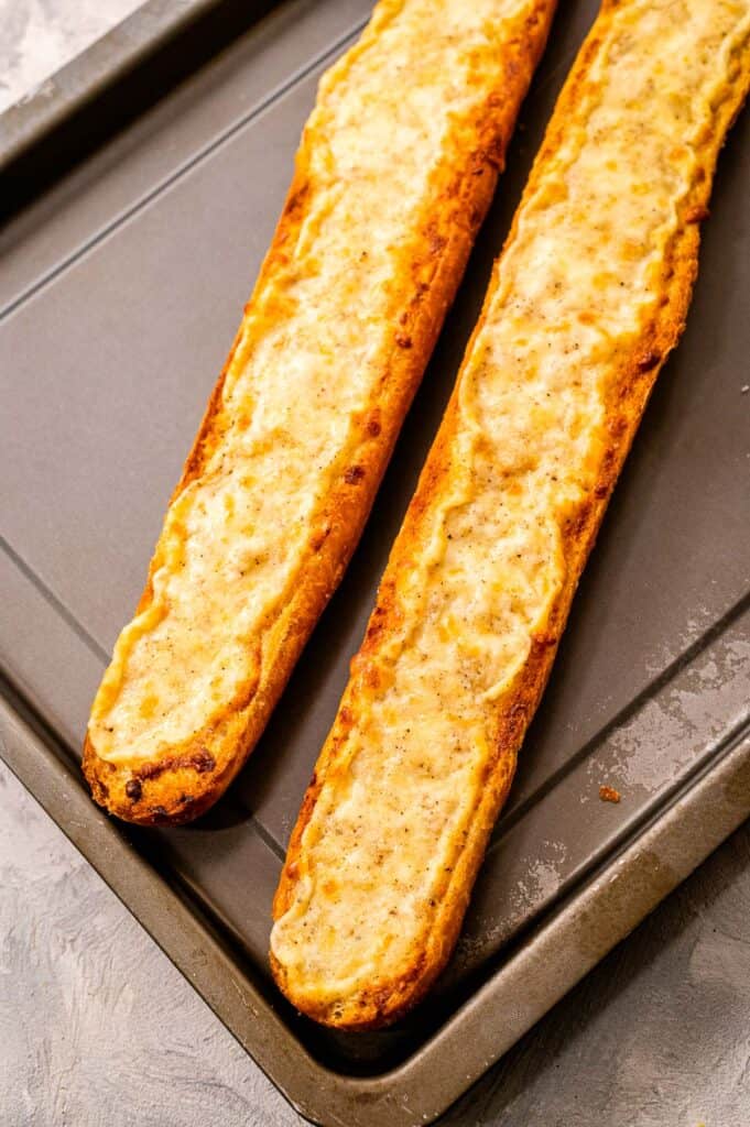 Baking sheet with two pieces of cheesy garlic bread on it