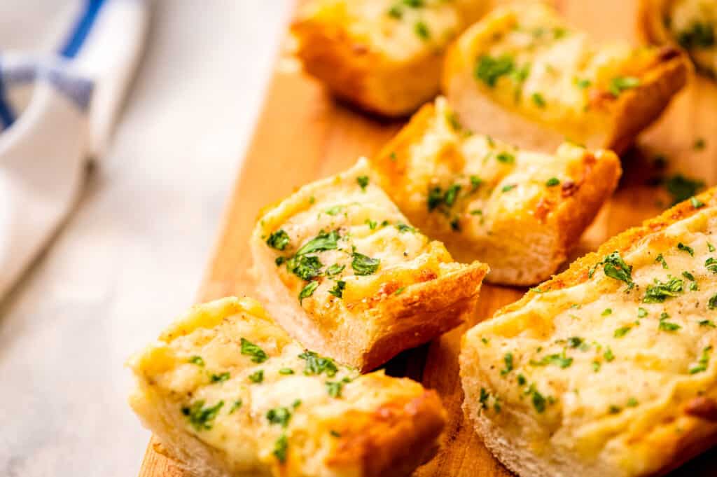 Sliced cheesy garlic bread on a wooden cutting board