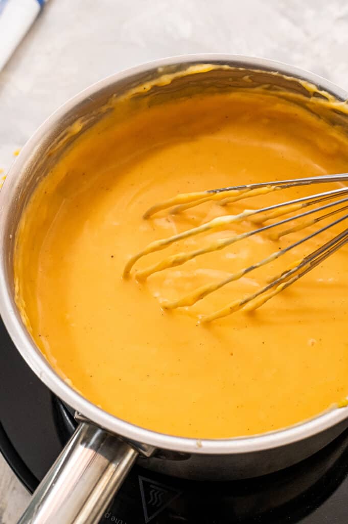 Whisking cheese sauce in saucepan with whisk.