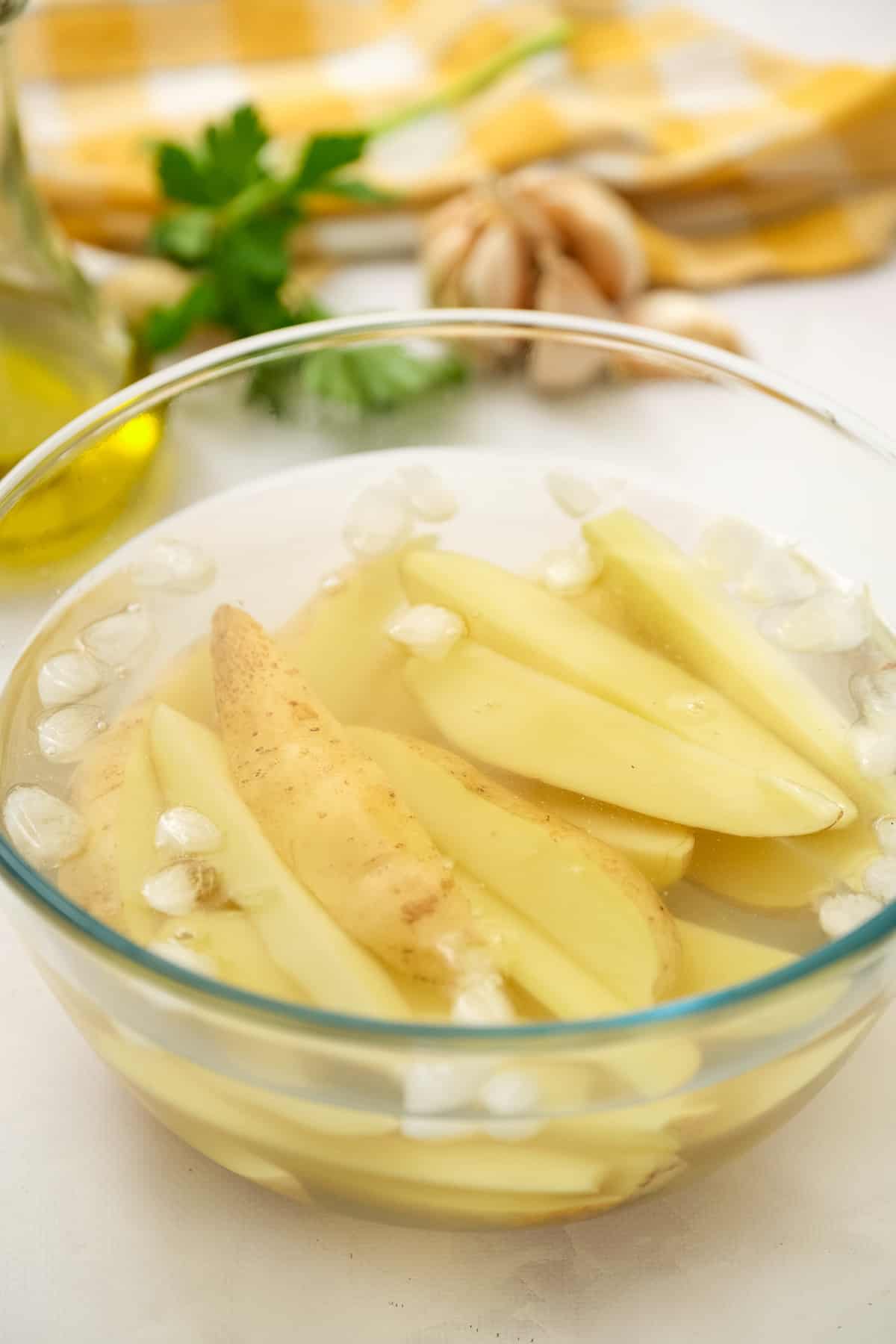 Glass bowl with water, ice cubes and potato wedges