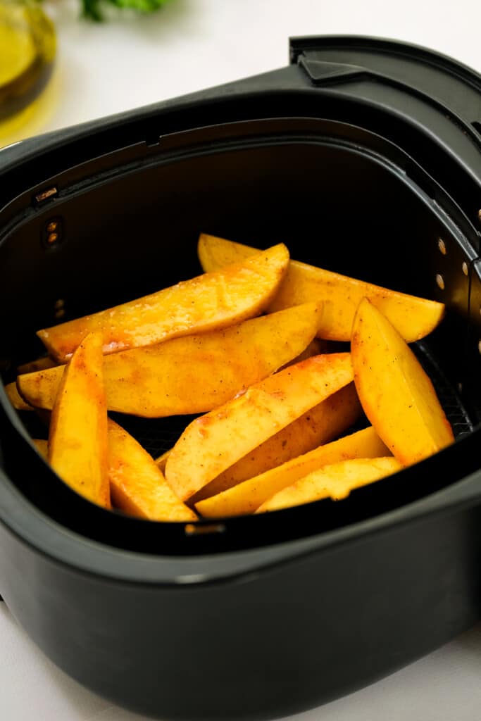 Raw potato wedges in air fryer basket