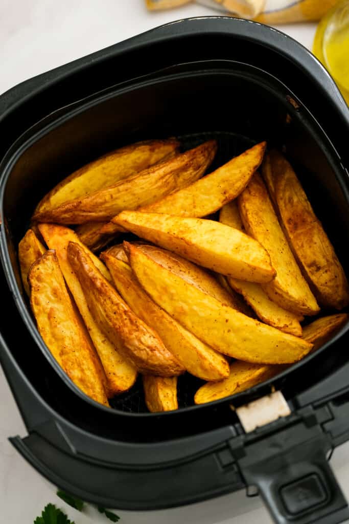 Cooked potato wedges in air fryer basket