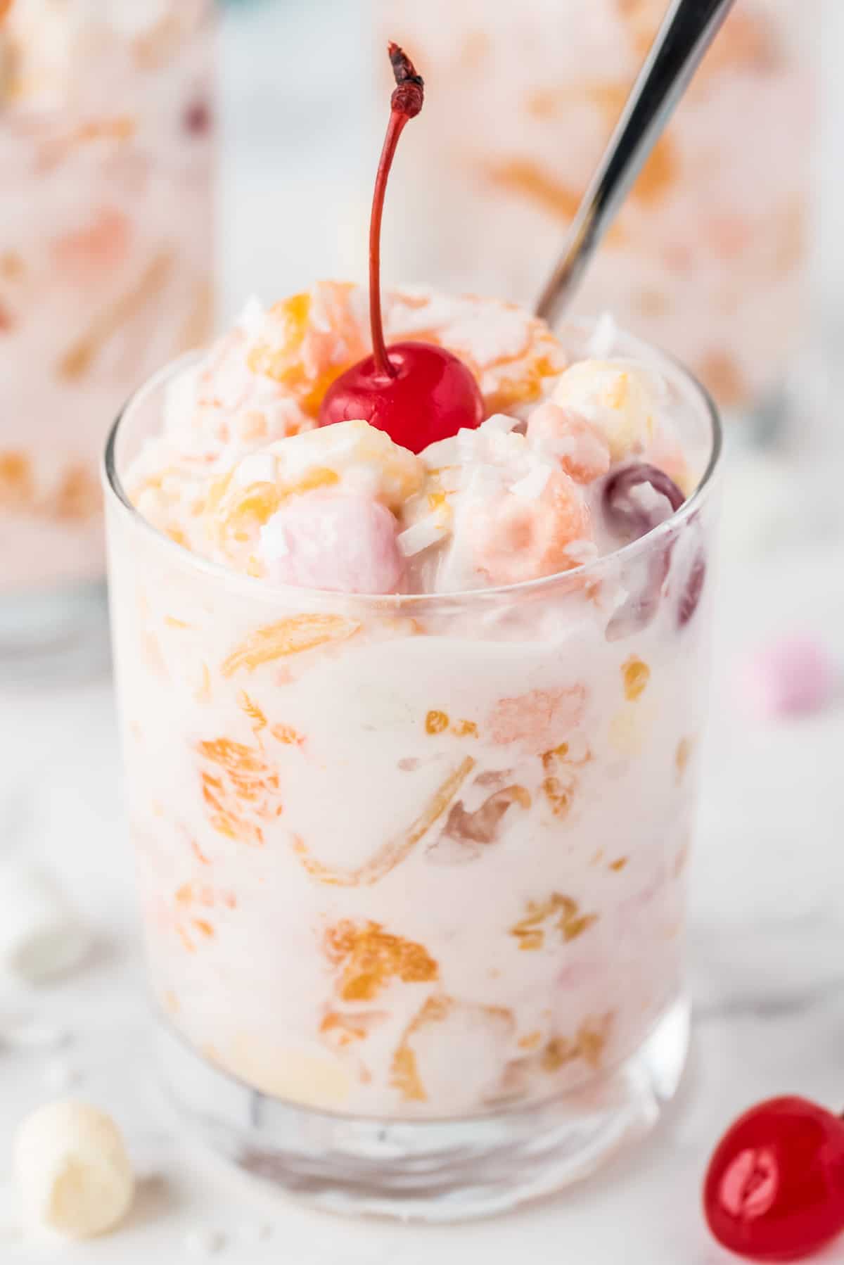 Small glass with Ambrosia Salad topped with maraschino cherry