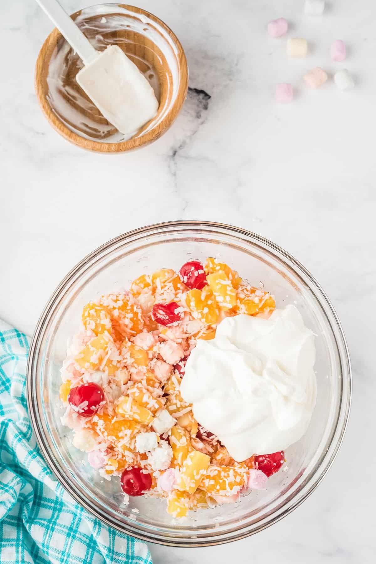 Overhead image of glass bowl with ingredients for Ambrosia salad with sour cream on top