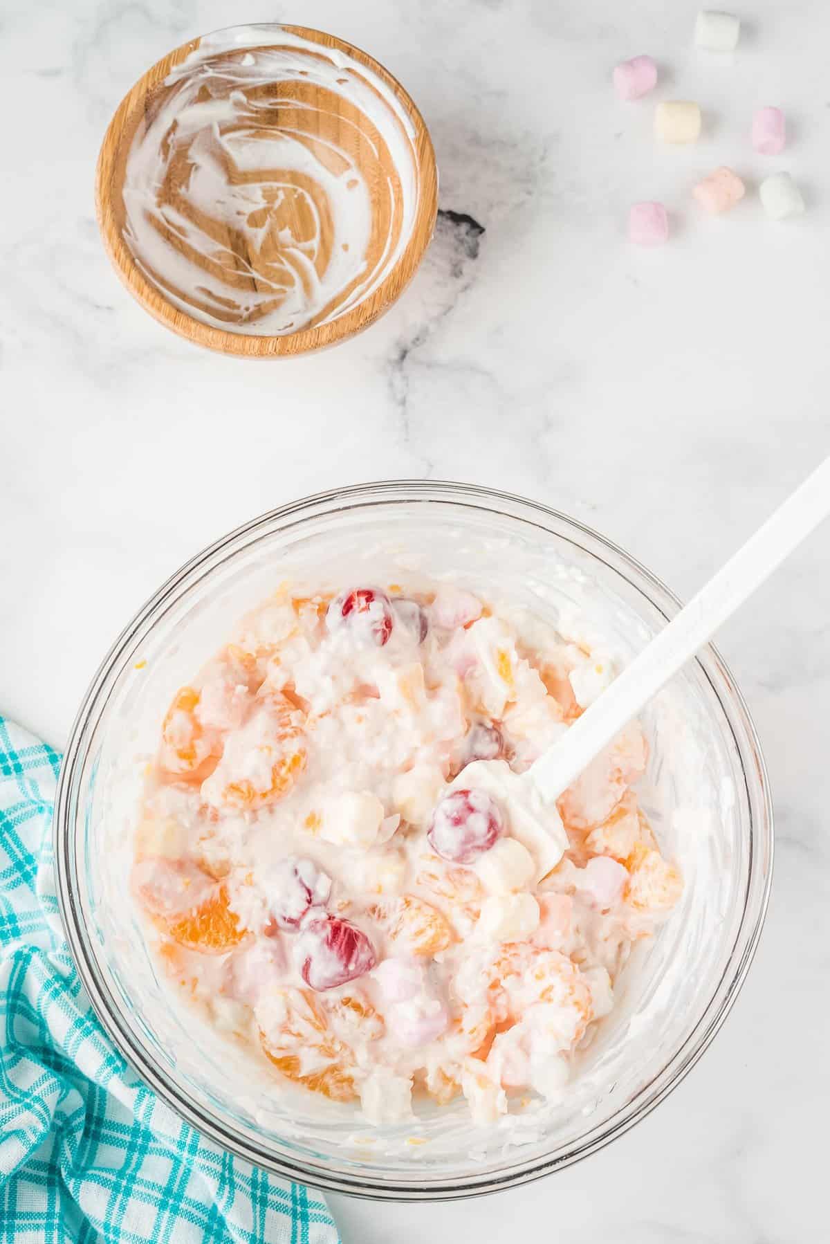 Overhead image of glass bowl with ingredients for Ambrosia salad with sour cream mixed in