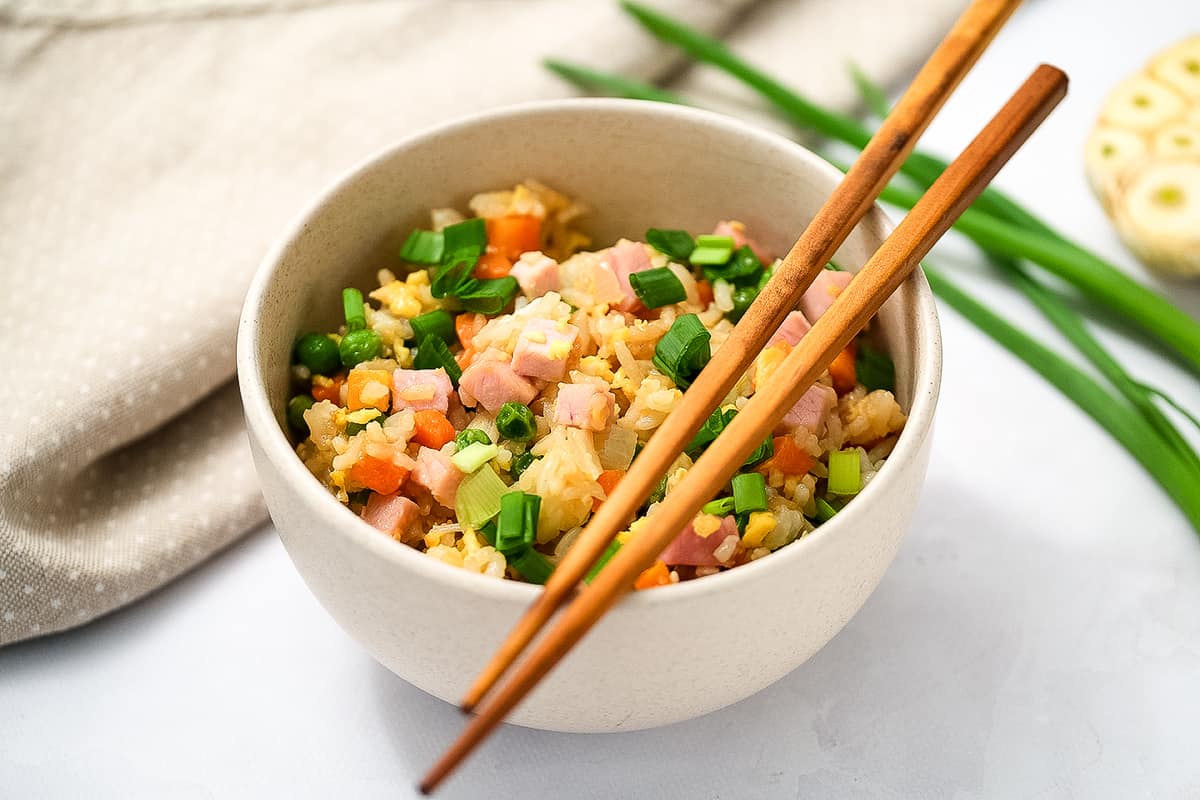 White bowl with ham fried rice and chopsticks on top