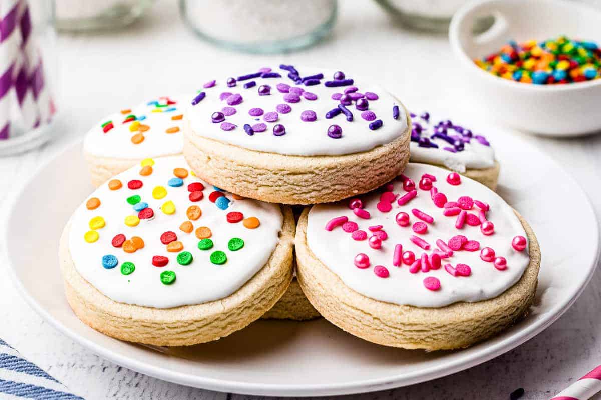Plate of white royal icing frosted round sugar cookies with sprinkles