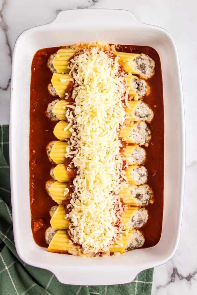 White casserole dish with stuffed manicotti pasta topped with cheese before baking