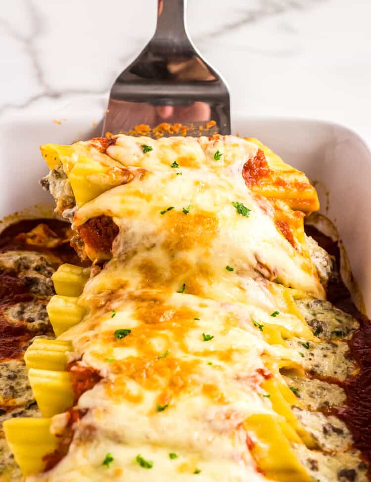 Spatula lifting Manicotti pasta out of casserole dish