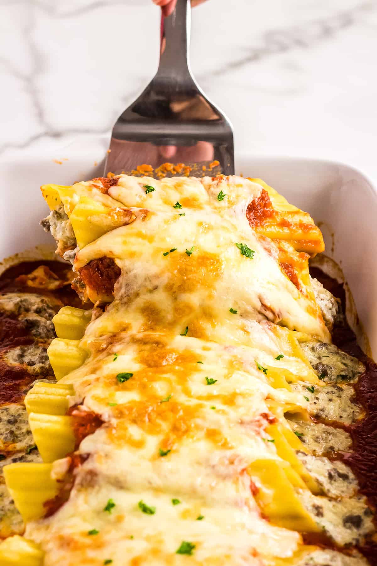 Spatula lifting Manicotti pasta out of casserole dish