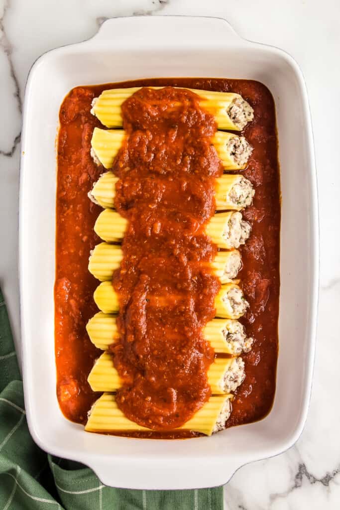 White casserole dish with stuffed manicotti pasta and spaghetti sauce over the top