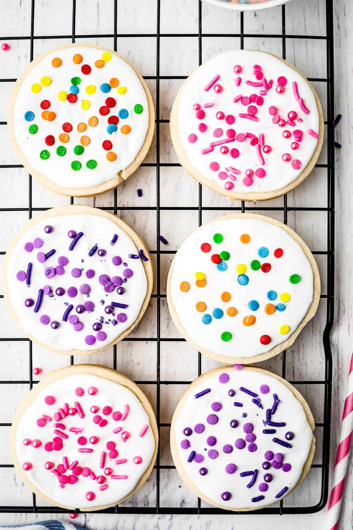 Round sugar cookies on baking rack decorated with royal icing and sprinkles