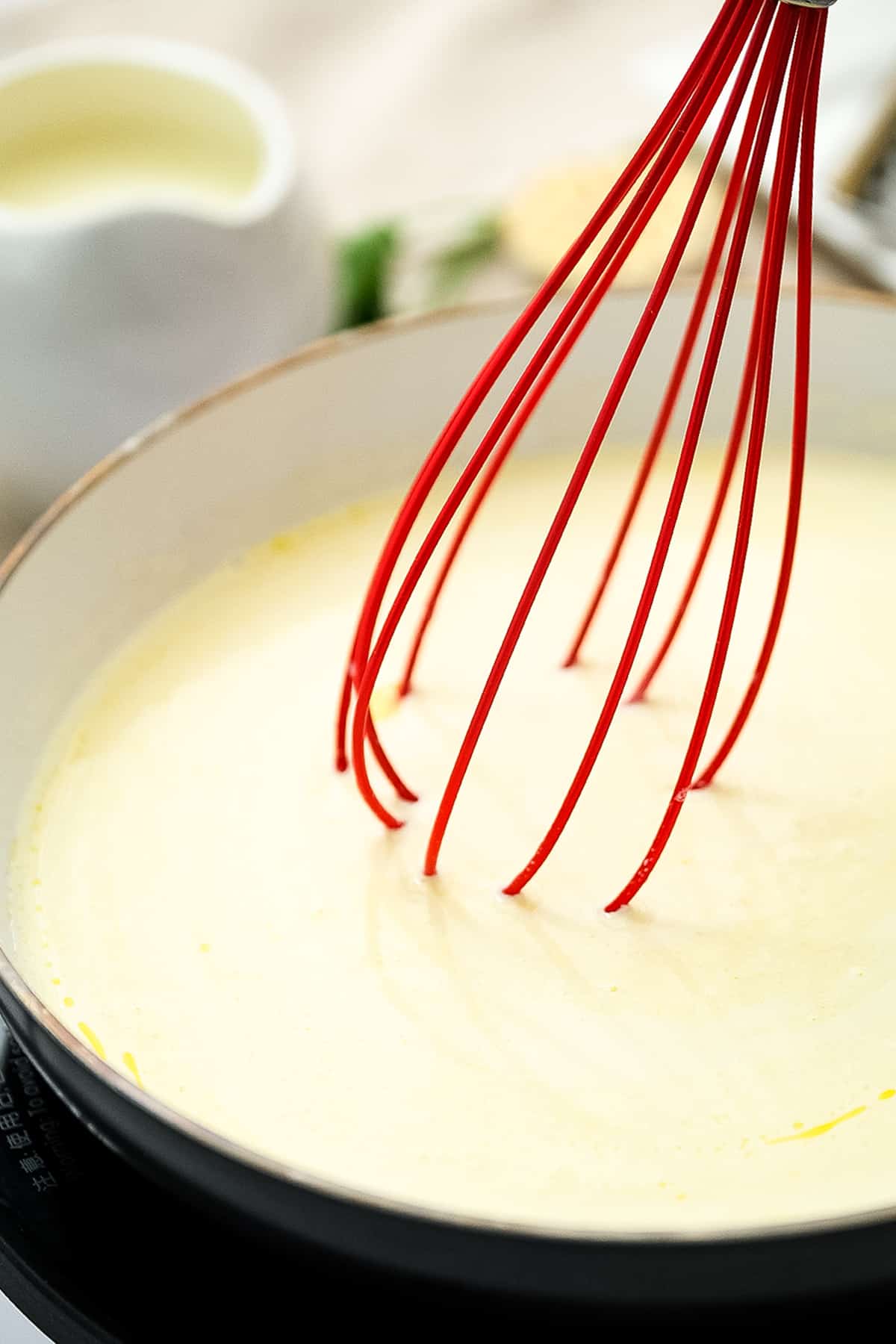 Skillet with Alfredo sauce and whisk mixing it