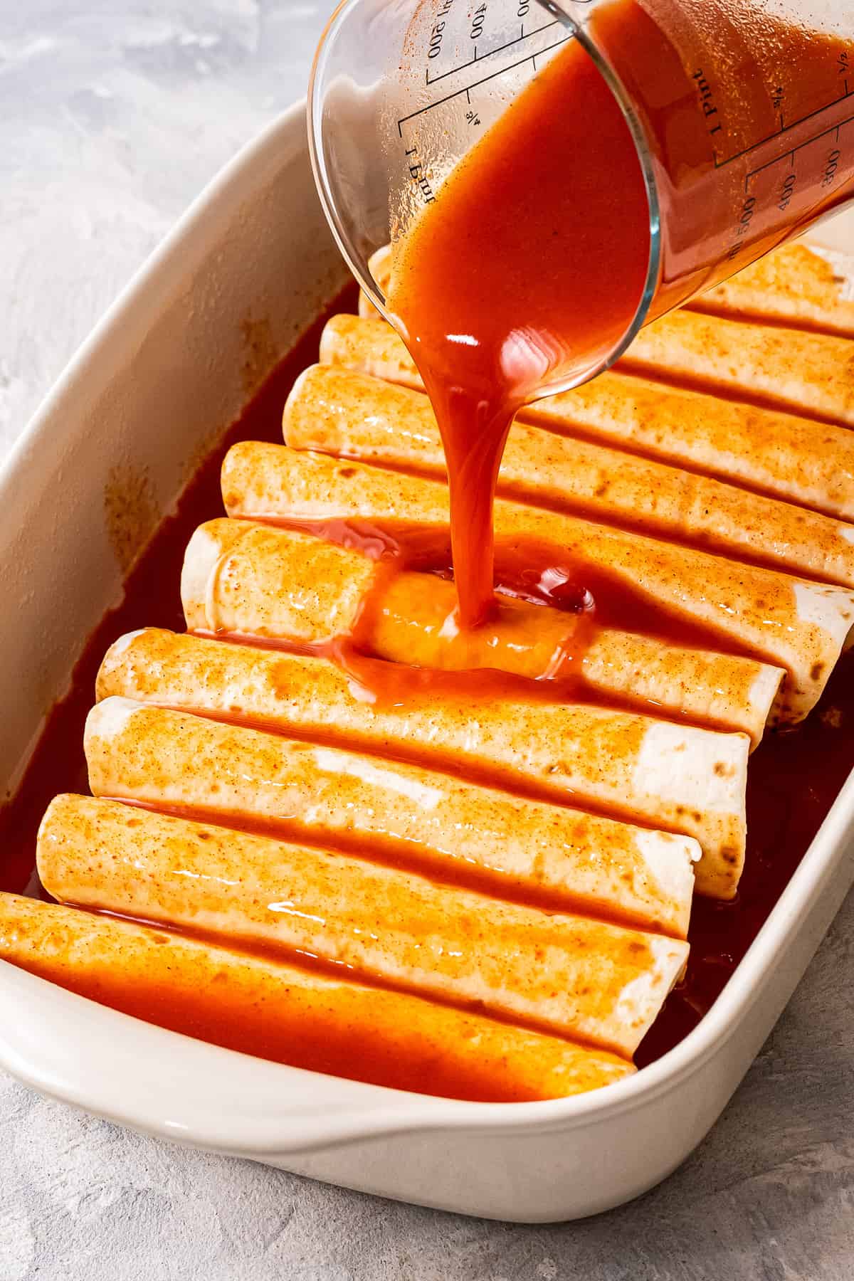 Pouring enchiladas sauce over tortillas in casserole dish