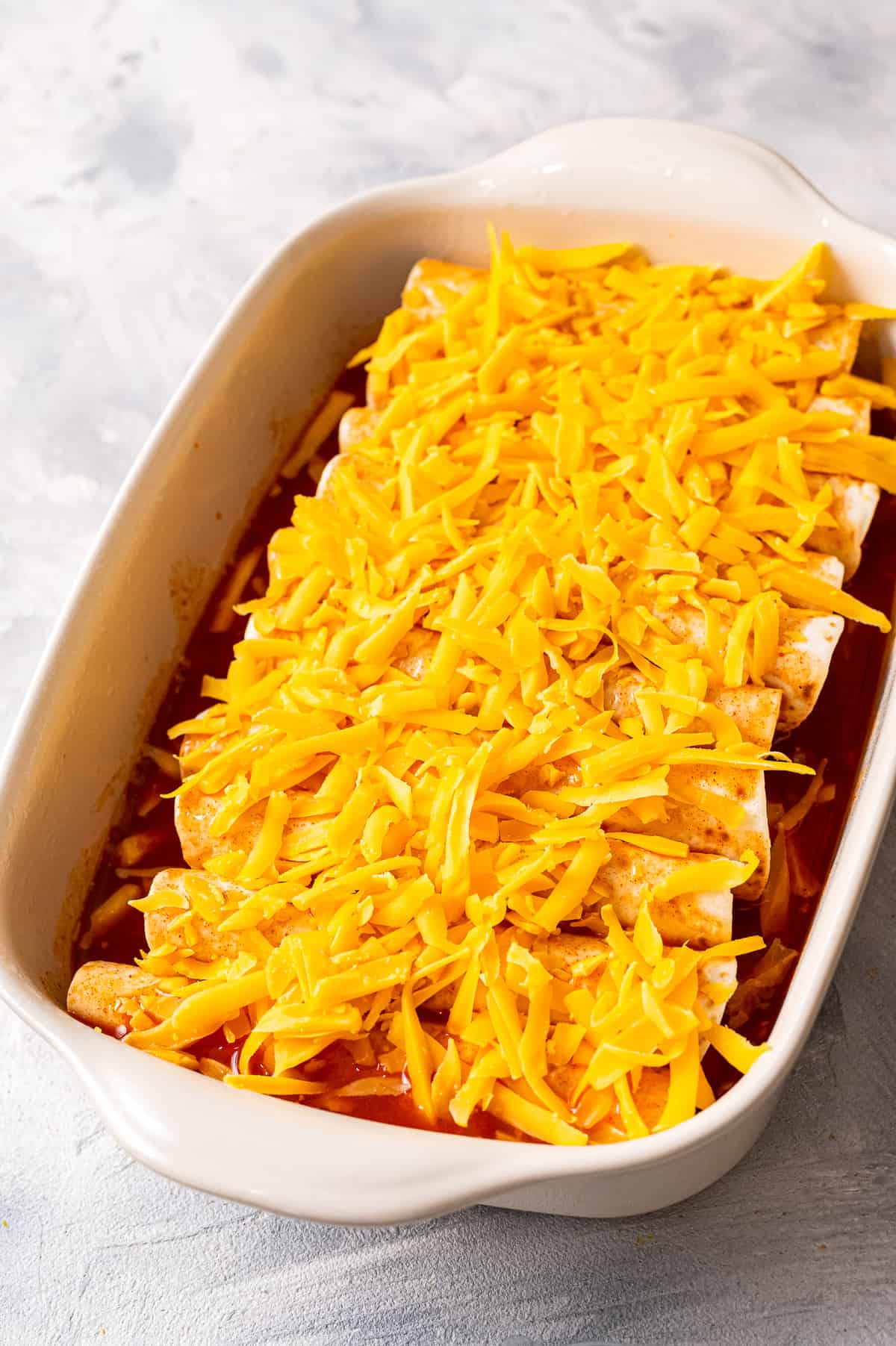 White casserole dish with ground beef enchiladas before baking