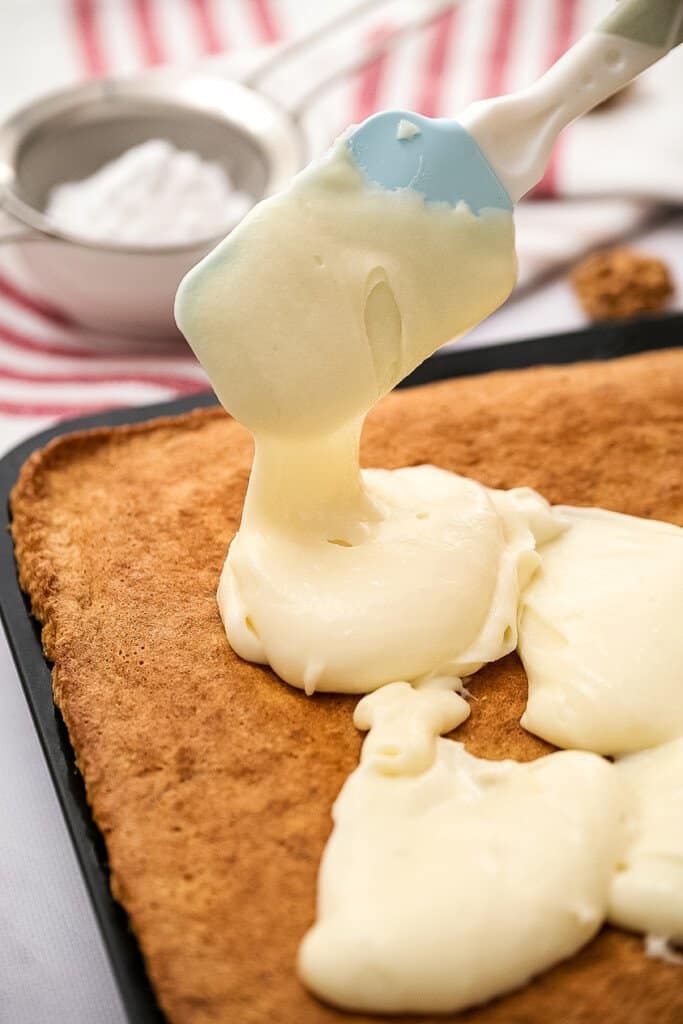 Pouring cream cheese frosting on top of carrot bars