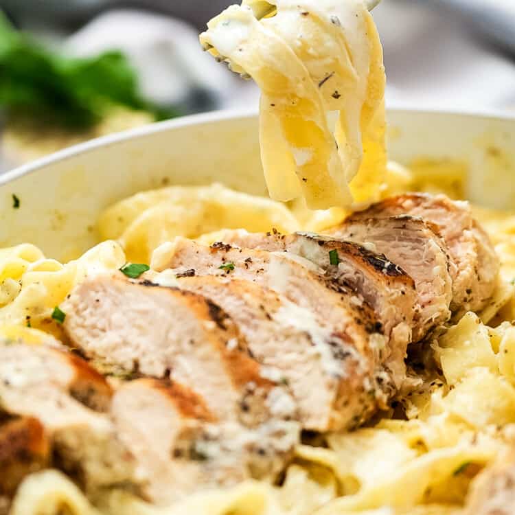 Fork twirling fettucine noodles out of a pan of chicken alfredo