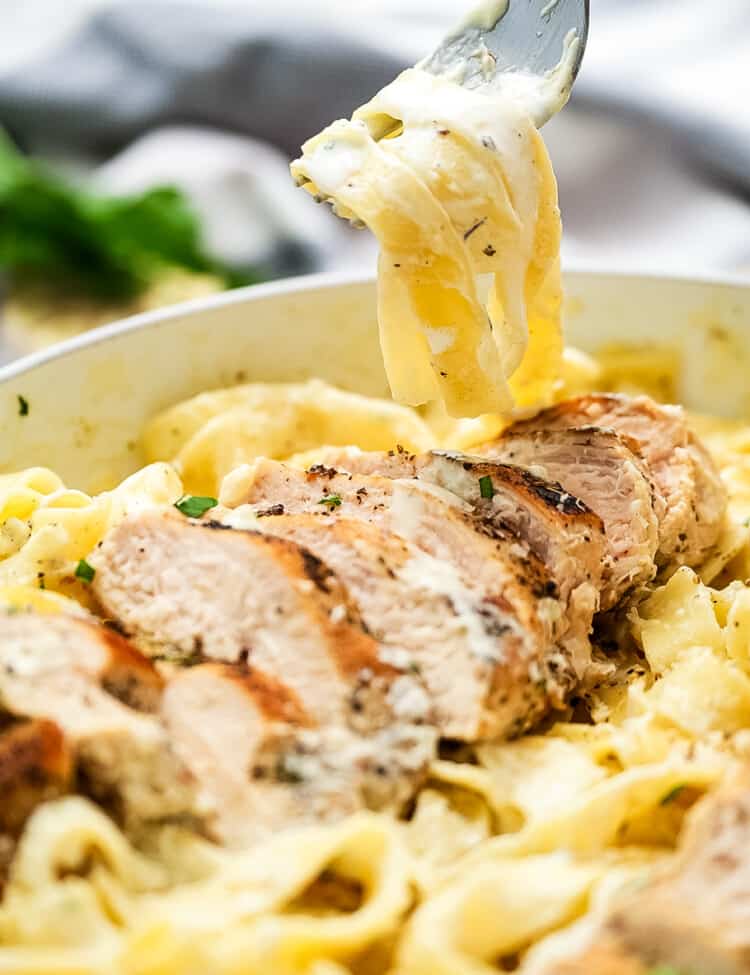 Fork twirling fettucine noodles out of a pan of chicken alfredo