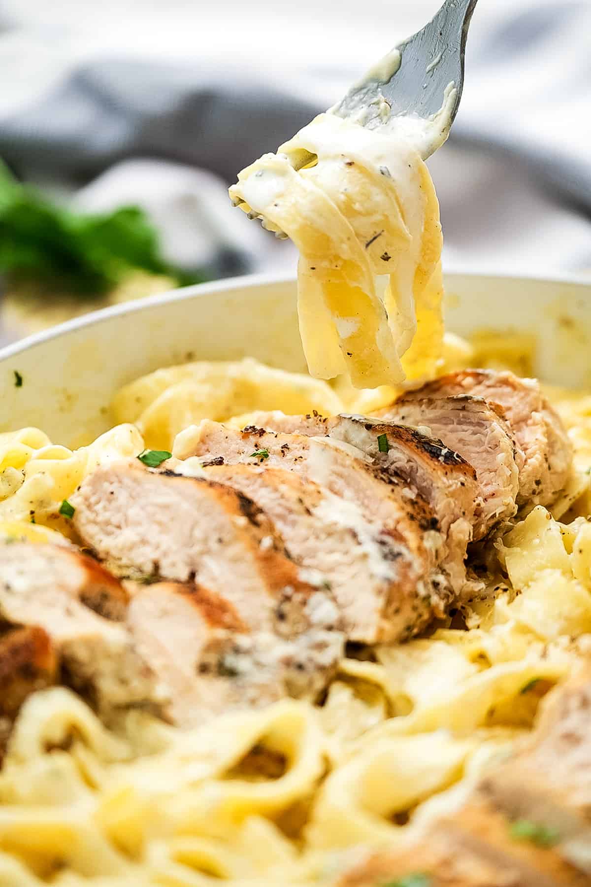 Fork twirling fettucine noodles out of a pan of chicken alfredo