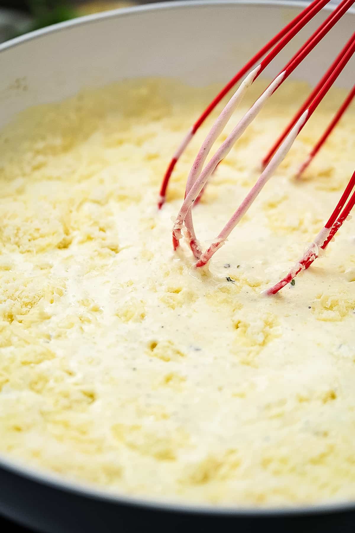 Whisk mixing cream sauce and shredded Parmesan cheese in skillet