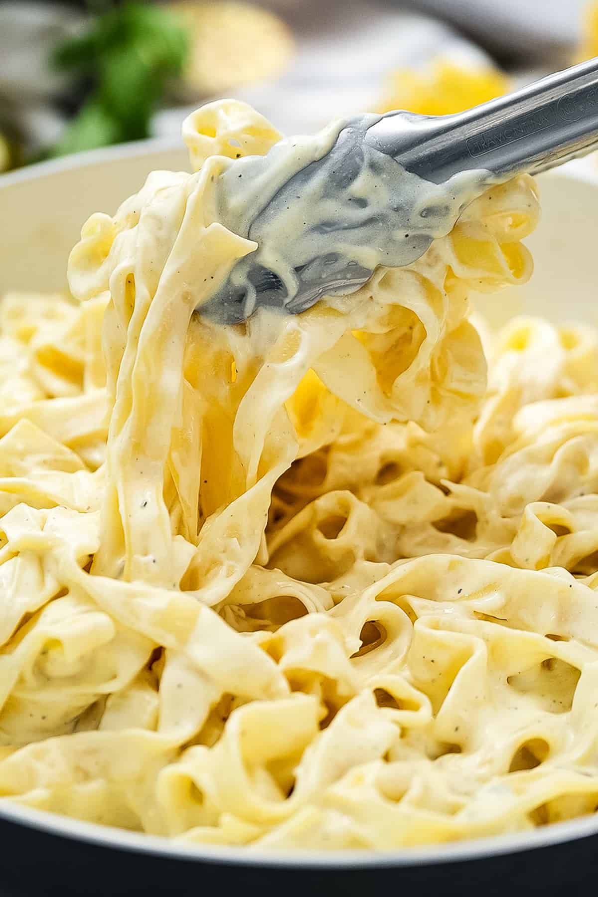 Tongs lifting linguine covered with Alfredo sauce