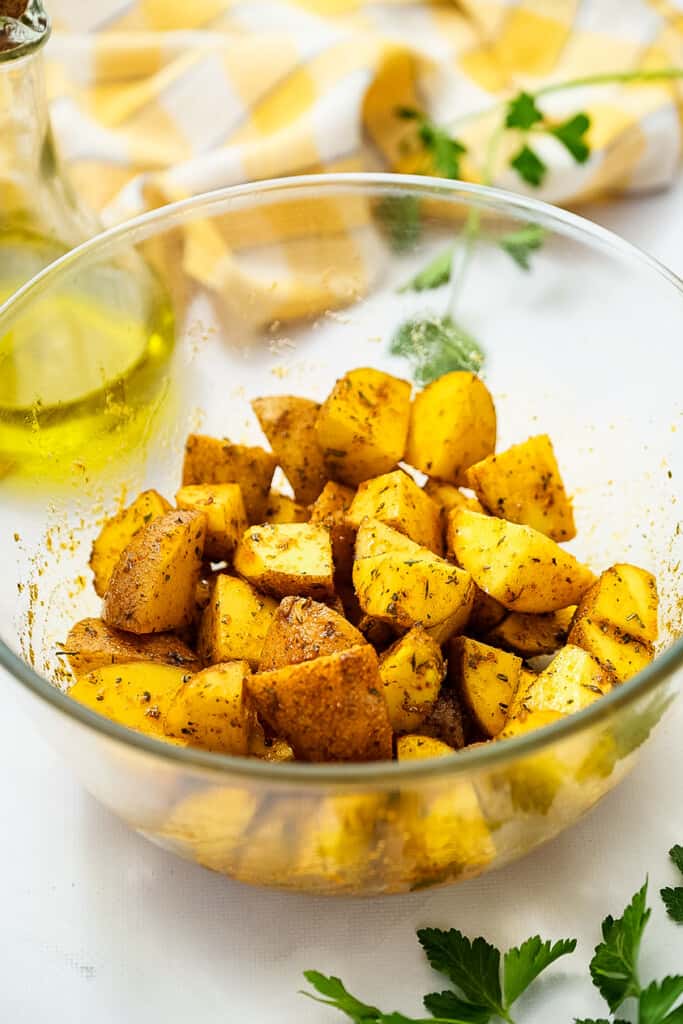 Glass bowl with diced potatoes in oil and seasonings